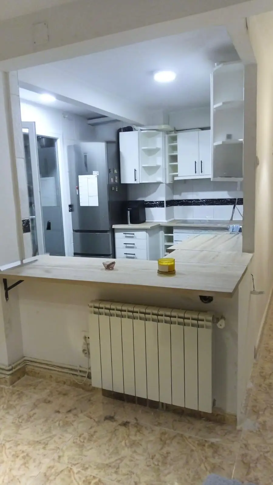 Reforma cocina con barra de madera clara abierta al salón y muebles blancos en Madrid