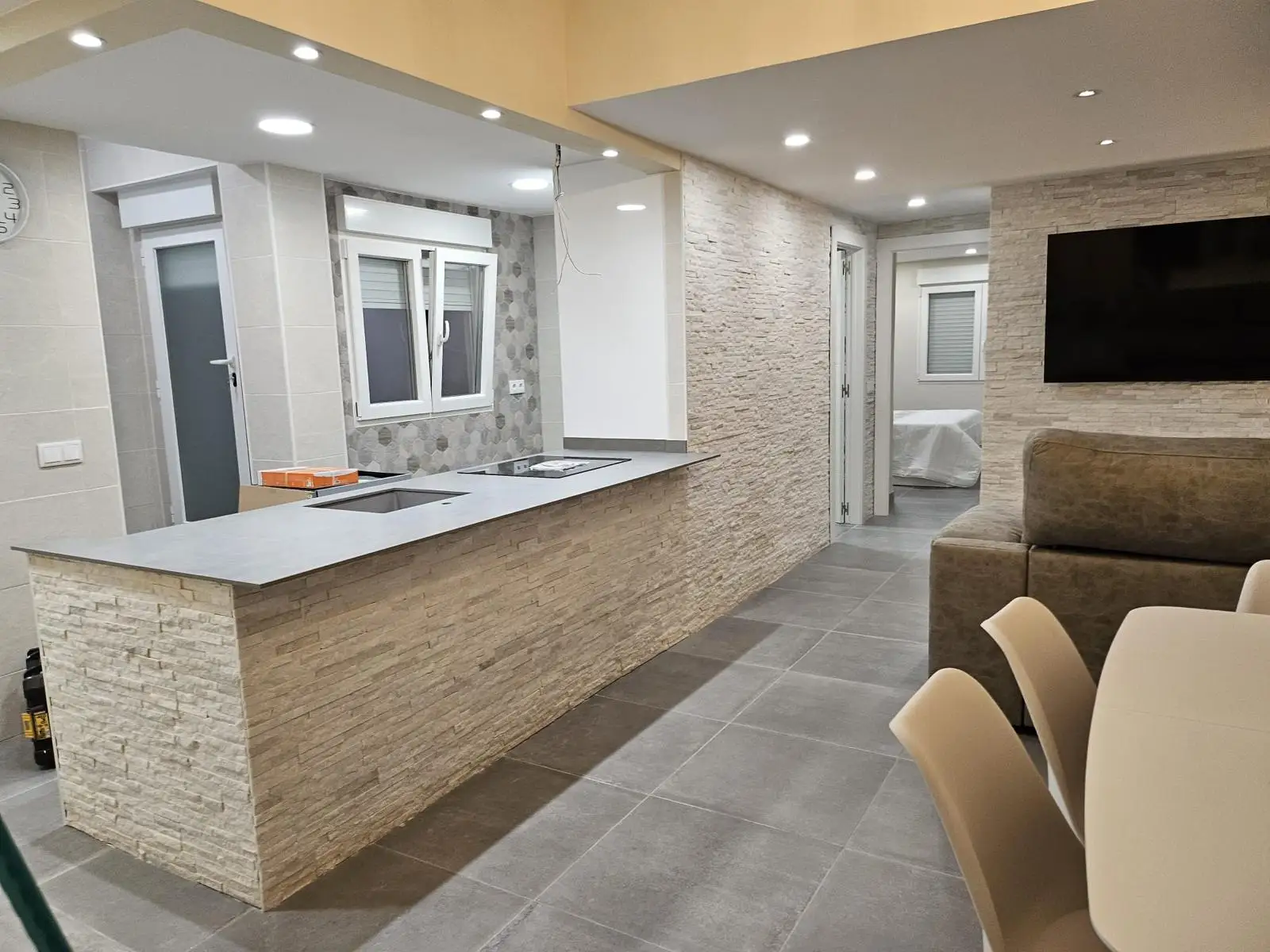 Reforma integral de vivienda con cocina abierta, barra de piedra decorativa y suelo porcelánico gris en Madrid