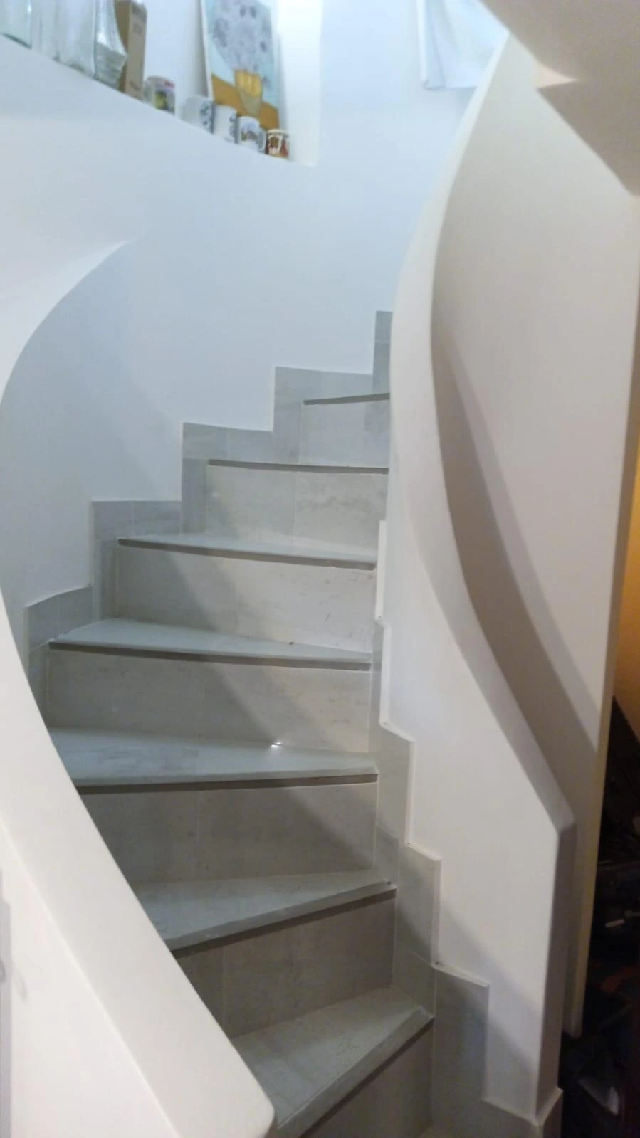 Reforma integral de escalera de caracol con peldaños cerámicos en tonos grises claros en Madrid