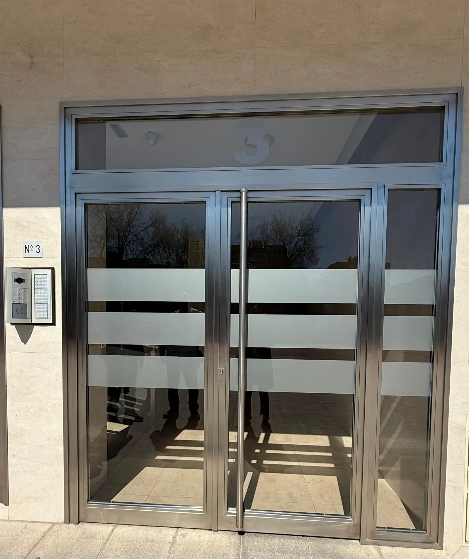 Rehabilitación de portal con puerta de acero inoxidable y cristales traslúcidos en Madrid